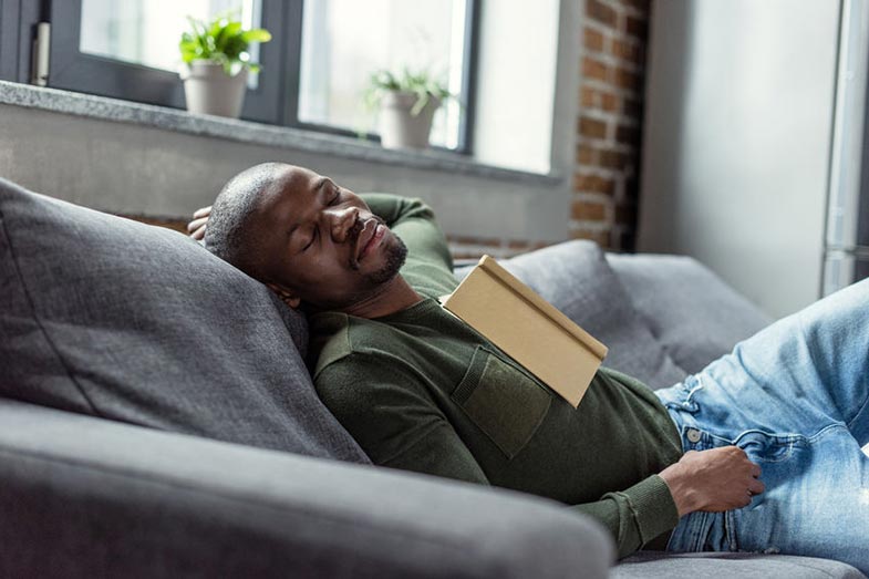 Man With Book Sleeping on Couch at Home