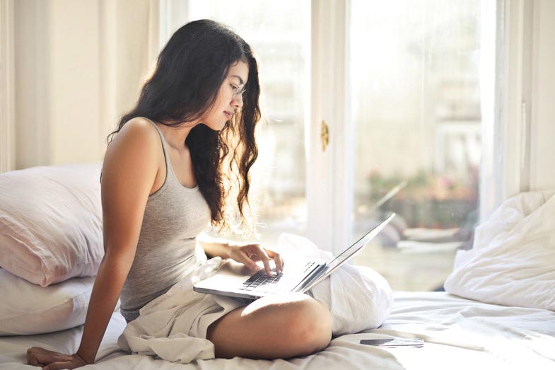 Woman in Gray Tank Top Using Laptop in Bed