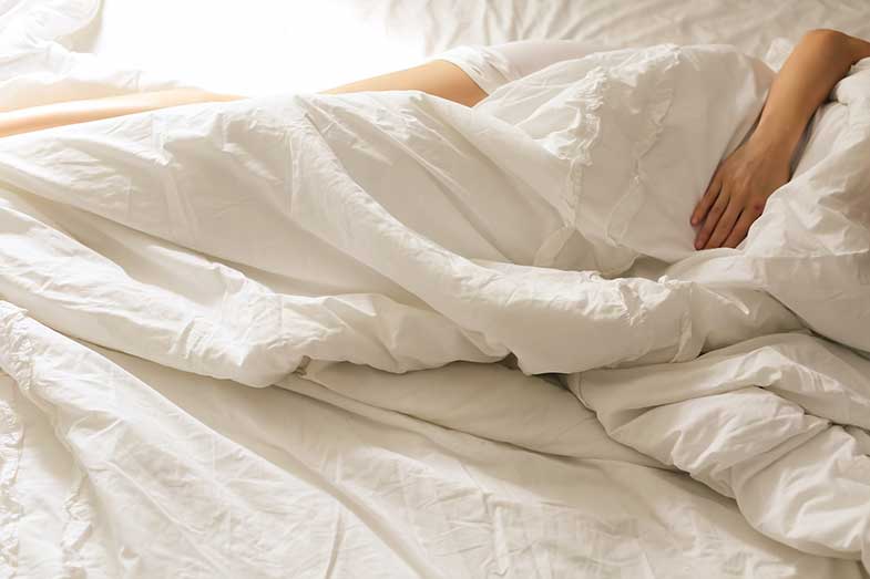 Woman Lying on Bed with White Sheets